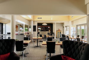 Un comedor de hotel con varias mesas y sillas, una zona de bar y vistas al exterior.