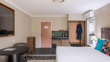 A hotel room with a bed, a desk, a chair, a TV, a kitchenette, and a bathroom.