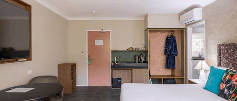 Habitación de hotel con cama, escritorio, silla, televisión, kitchenette y baño.