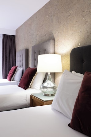 A hotel room with two beds, a nightstand with a lamp, and a textured wall. - Mandala Signature Berry (Berry)