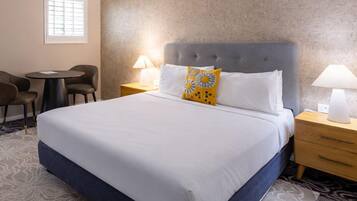 A hotel room with a large bed, two bedside tables, a chair, and a small table.