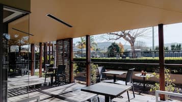 An outdoor patio with tables and chairs, a view of the surrounding area, and a covered section with a slatted wall.