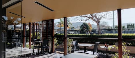An outdoor patio with tables and chairs, a view of the surrounding area, and a covered section with a slatted wall.