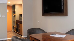 A dining area with a wooden table and four grey chairs, a flat-screen TV mounted on the wall, and a closet with a sliding door in the background.