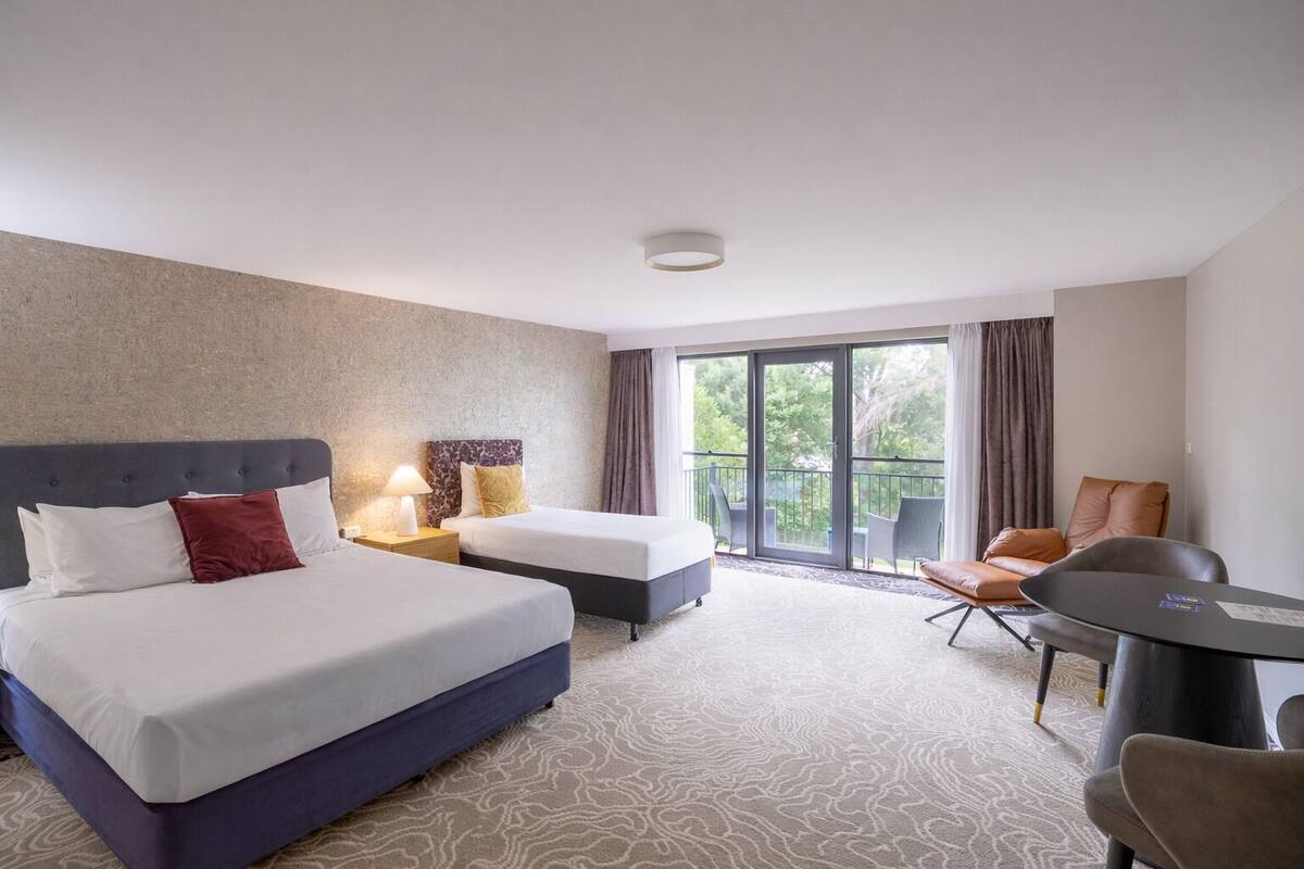 A hotel room with two beds, a balcony, a dining table, and a chair.