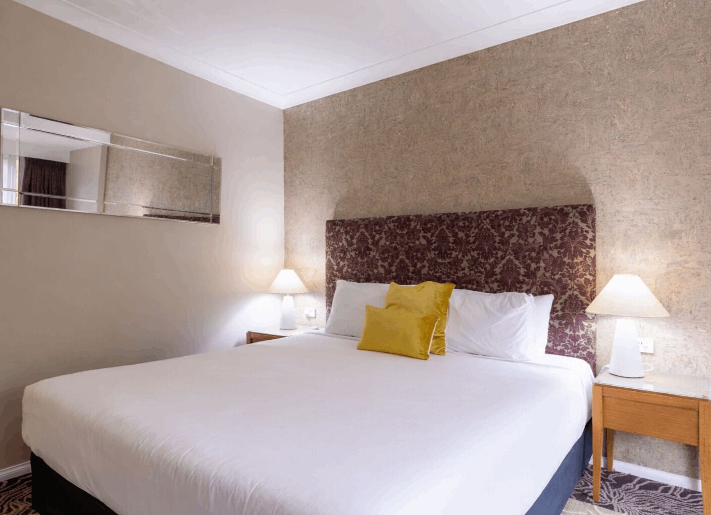 A hotel room with a large bed, two bedside tables, a mirror, and a patterned headboard.