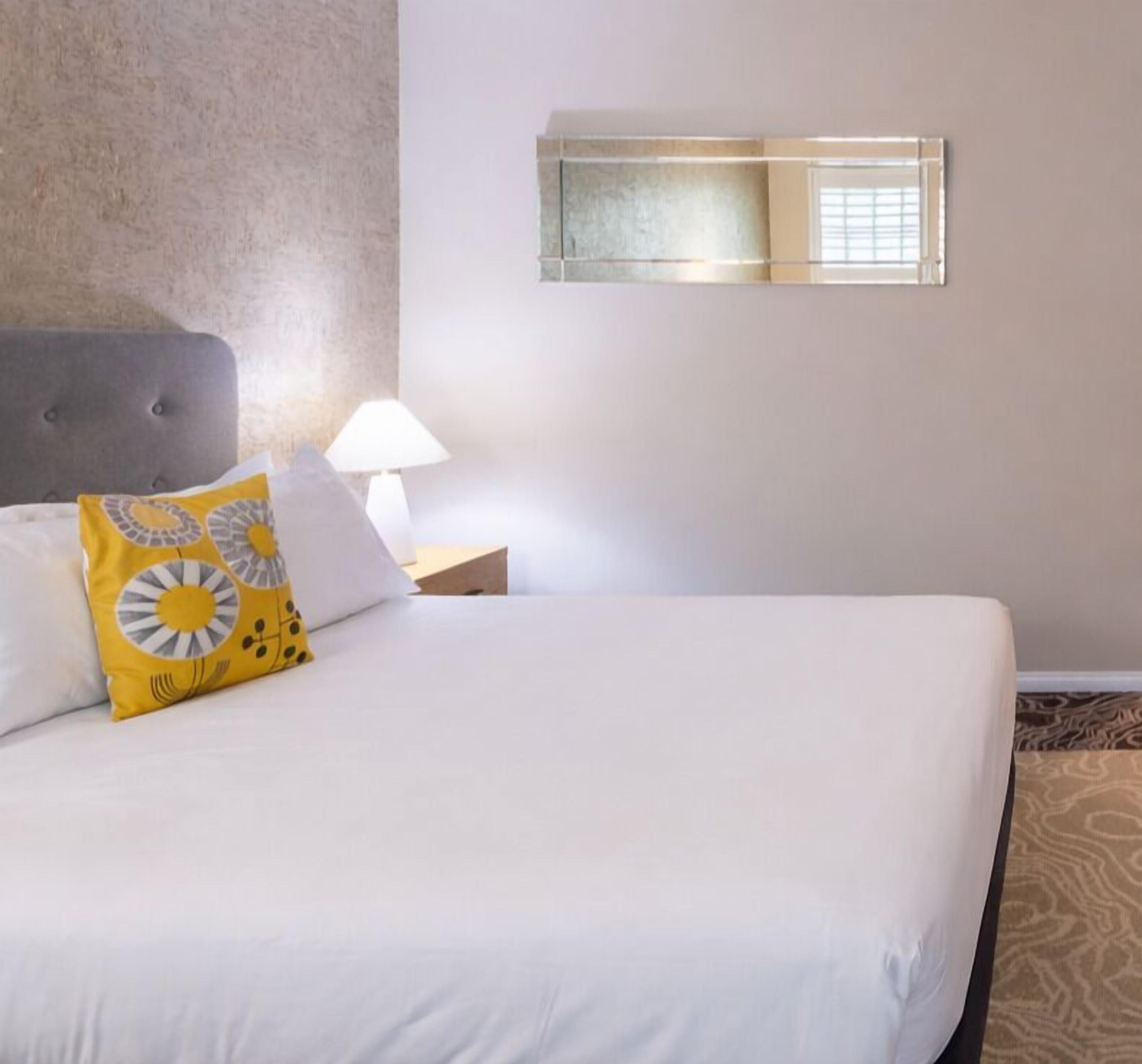 Una habitación de hotel con cama, mesita de noche, lámpara y ventana con persianas.