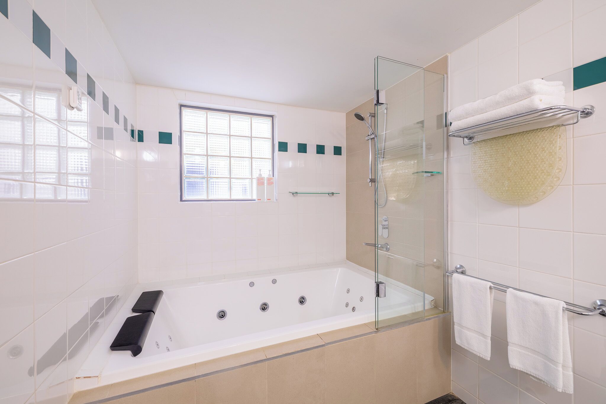 A modern bathroom with a glass-enclosed shower, a bathtub with controls, and a window providing natural light.