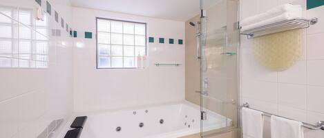 A modern bathroom with a glass-enclosed shower, a bathtub with controls, and a window providing natural light.