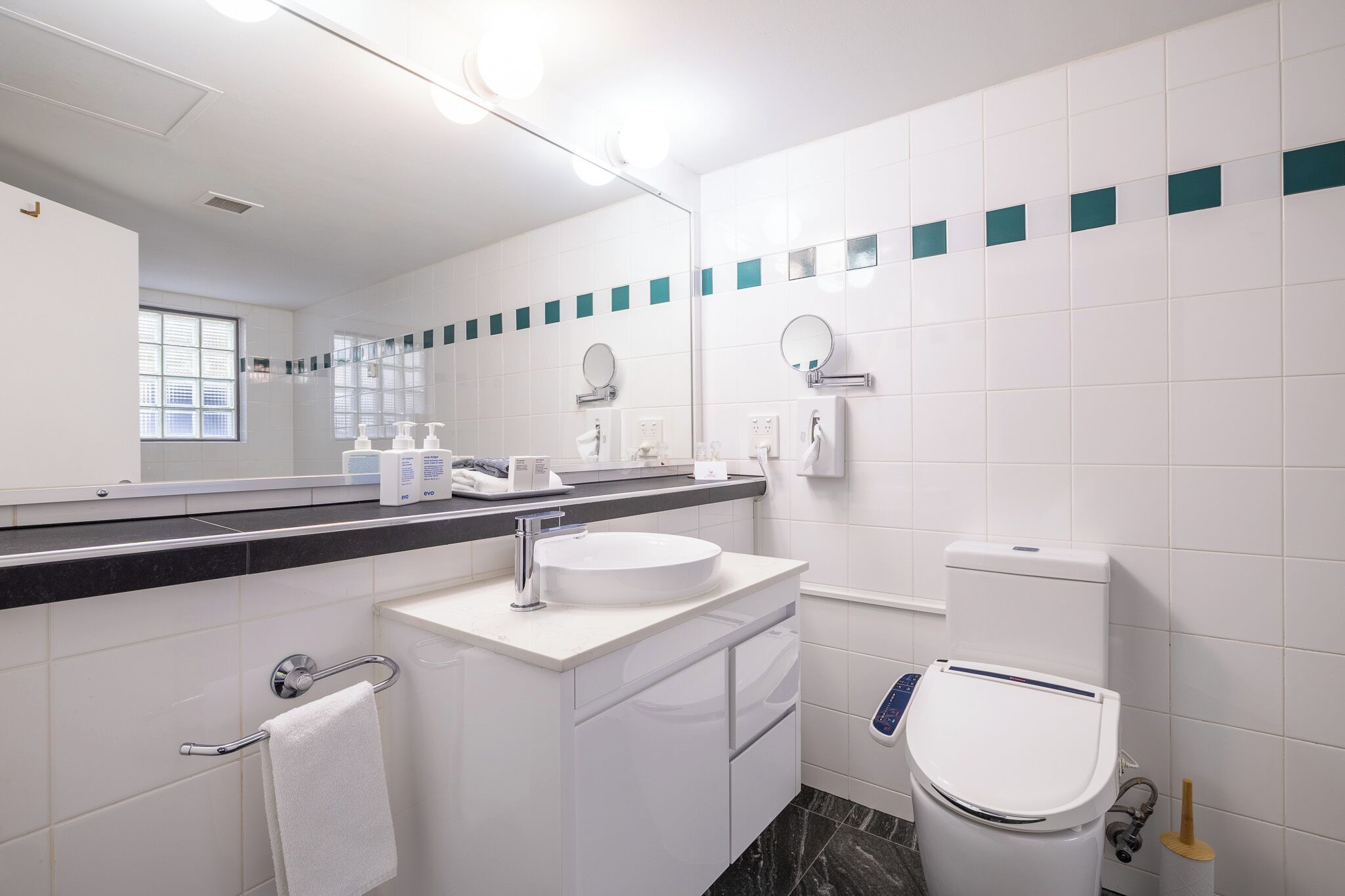 Un baño moderno con lavamanos, espejo y inodoro blancos.
