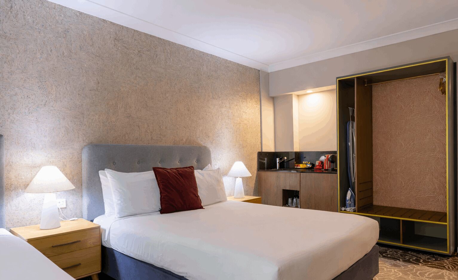 A hotel room with a bed, bedside tables, a nightstand, a wardrobe, and a mirror.