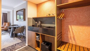 A modern hotel room with a dining area, a kitchen with a black countertop, and a wooden wall with a unique pattern.