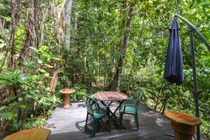 An outdoor wooden deck with a table and chairs surrounded by dense foliage.