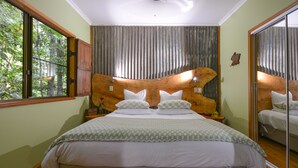 Un dormitorio con una cama grande, cabecera de madera, un espejo grande y una ventana con vistas a árboles.
