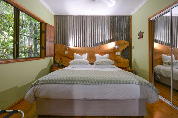 A bedroom with a large bed, a wooden headboard, a large mirror, and a window with a view of trees.