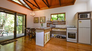 Una cocina con piso de madera, una isla central, estufa, microondas y refrigerador. Hay sillas y una mesa afuera de la ventana.