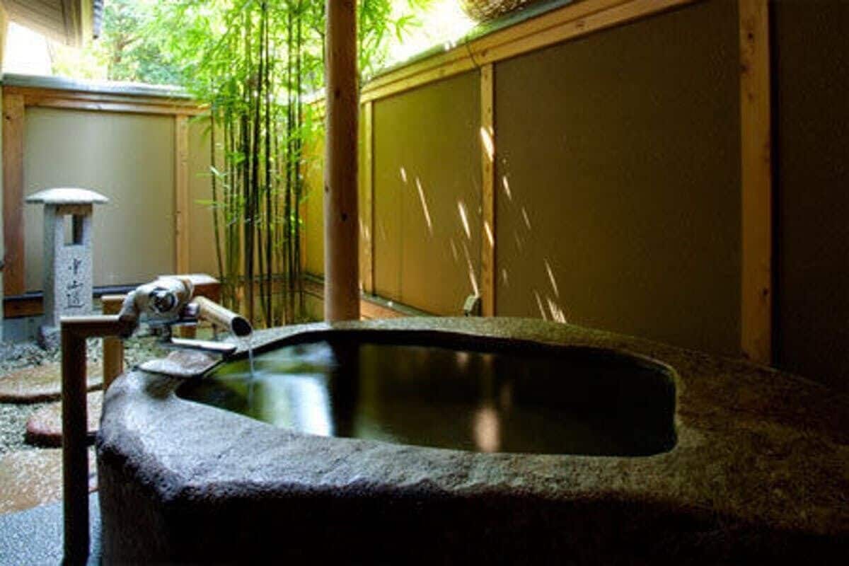 A stone hot spring with a wooden structure, bamboo, and a traditional Japanese screen.