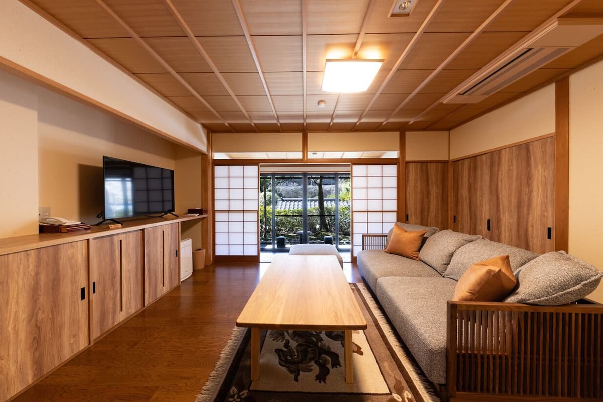 A traditional Japanese room with tatami flooring, a low wooden table, a sofa with cushions, and a television on a cabinet.