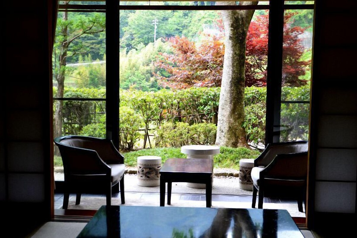 A room with a view of a garden through large windows, featuring a table and two chairs.