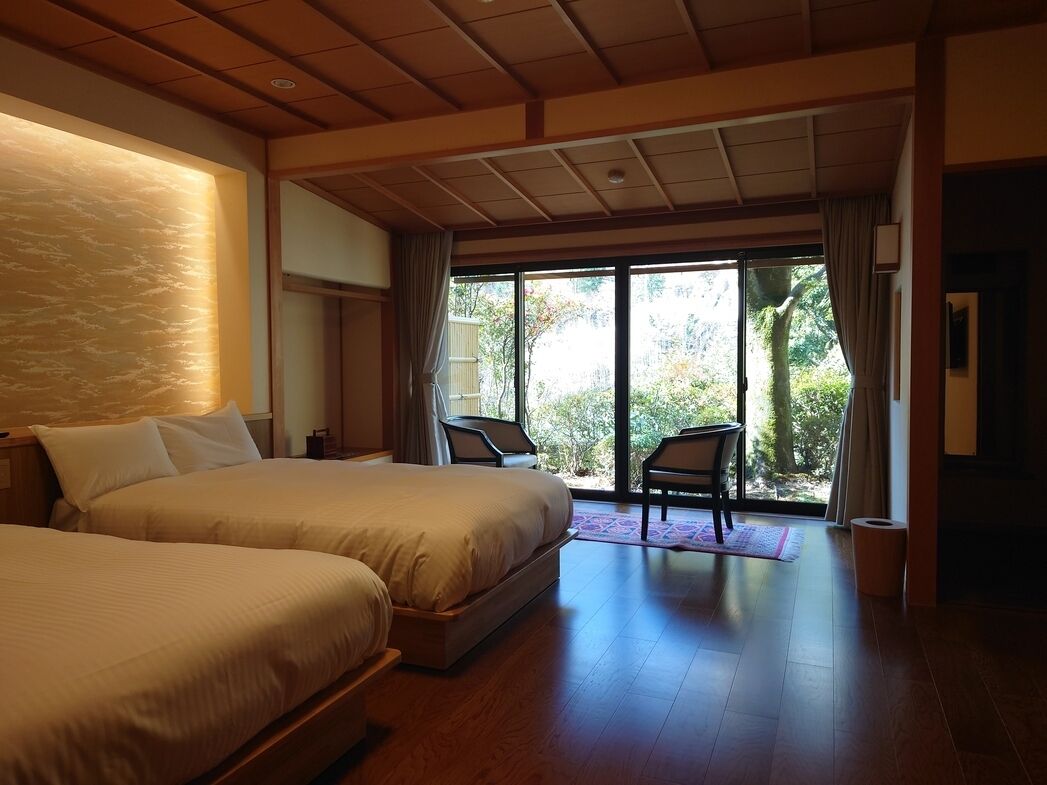 Ein Hotelzimmer mit zwei Betten, einem großen Fenster und Blick auf Grün.