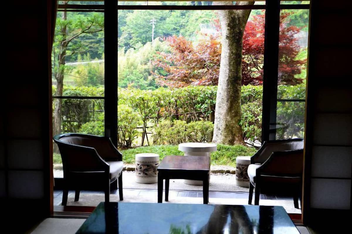 A room with a view of a garden through large windows, featuring a table and two chairs.