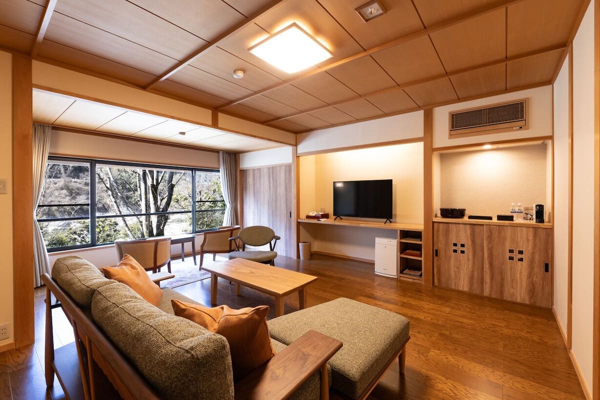 A modern living room with a sofa, chairs, a TV, and a kitchen area with cabinets and a microwave.
