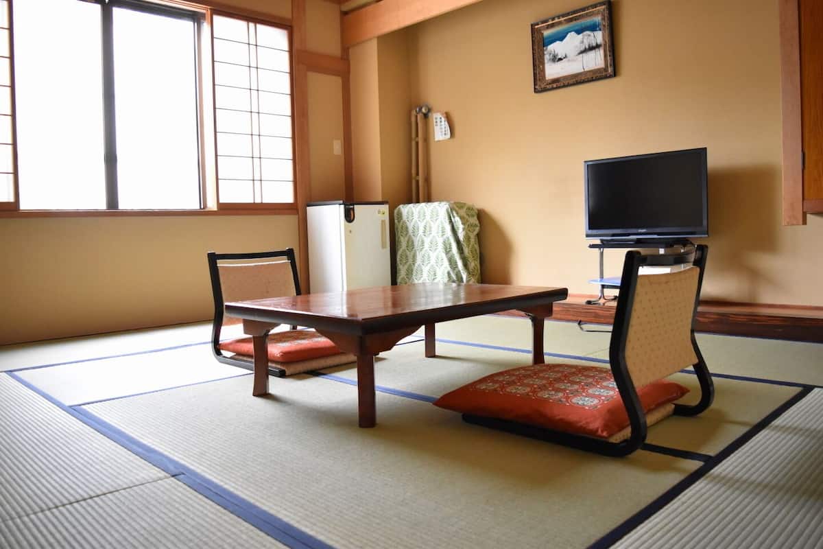 Una habitación con tatami, una mesa baja, dos sillas, un televisor y un cuadro en la pared.