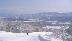 A snowy landscape with a clear sky, a person skiing, and distant mountains. - Uesugi Kenshinnokakushiyu Sekionsen Asahiya Ryokan (Myoko)