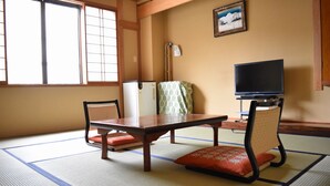 A tatami mat room with a low table, two chairs, a television, and a picture on the wall. - Uesugi Kenshinnokakushiyu Sekionsen Asahiya Ryokan (Myoko)