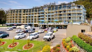 A multi-story hotel with a central courtyard, outdoor seating, and a parking lot. - Bali in Broughton (Nelson Bay)