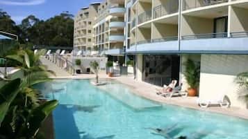 Una piscina con sillones de descanso y un edificio de varios pisos al fondo.