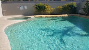 A clear swimming pool with a sandy edge, surrounded by a low wall with warning signs.