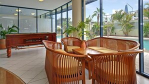 A spacious indoor area with large windows, a wooden bench, and wicker chairs. - Bali in Broughton (Nelson Bay)