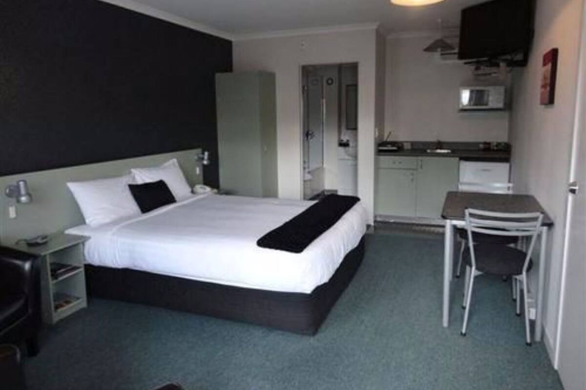 A hotel room with a bed, bedside table, chair, and kitchenette.