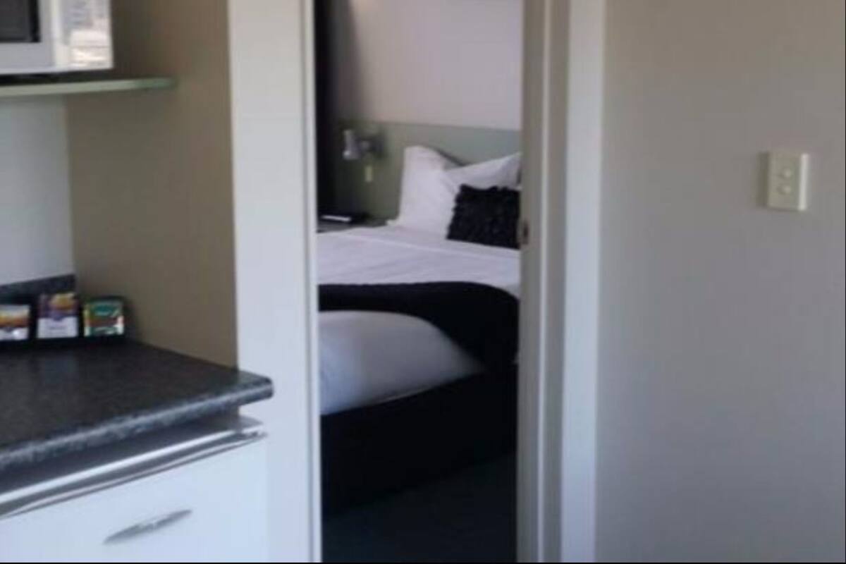 A hotel room with a bed, a nightstand, and a small shelf with items.