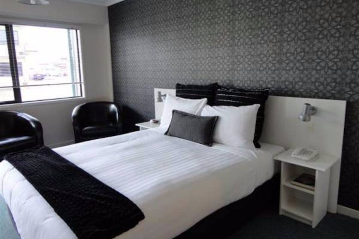 A hotel room with a large bed, a nightstand, a chair, and a window with a view.