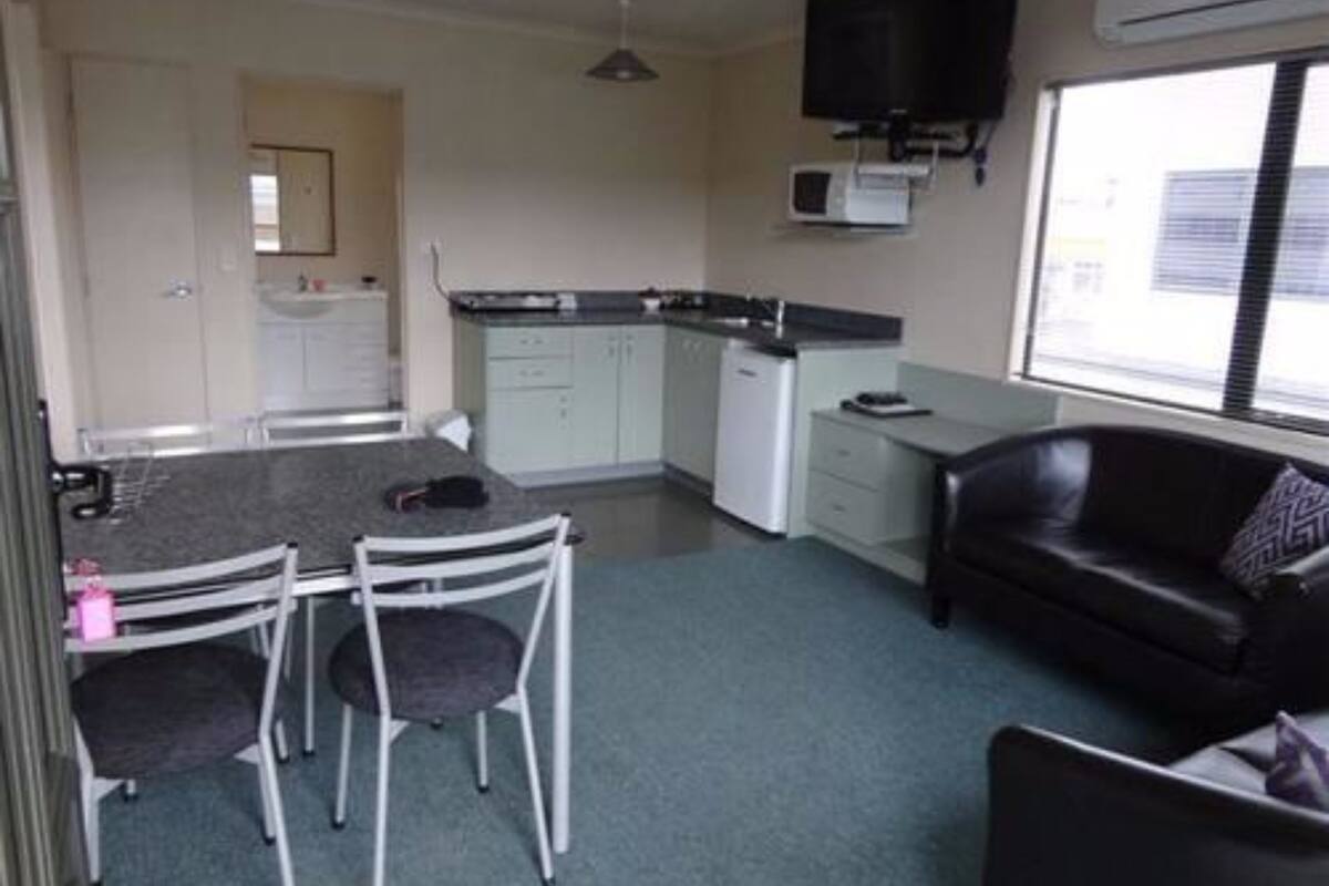 A compact living space with a kitchenette, a dining area with chairs, a sofa, and a TV mounted on the wall.