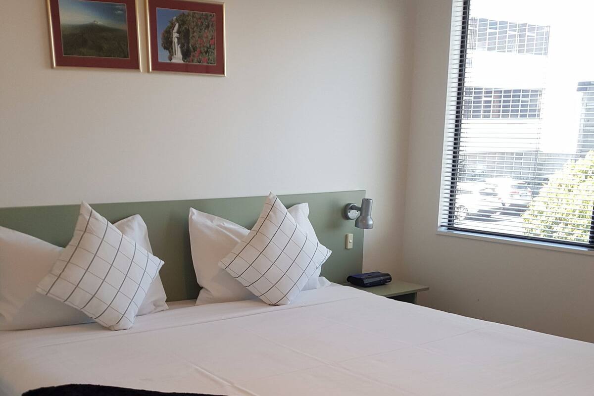 A neatly made bed with white linens and black trim, a green headboard, and two framed pictures on the wall.