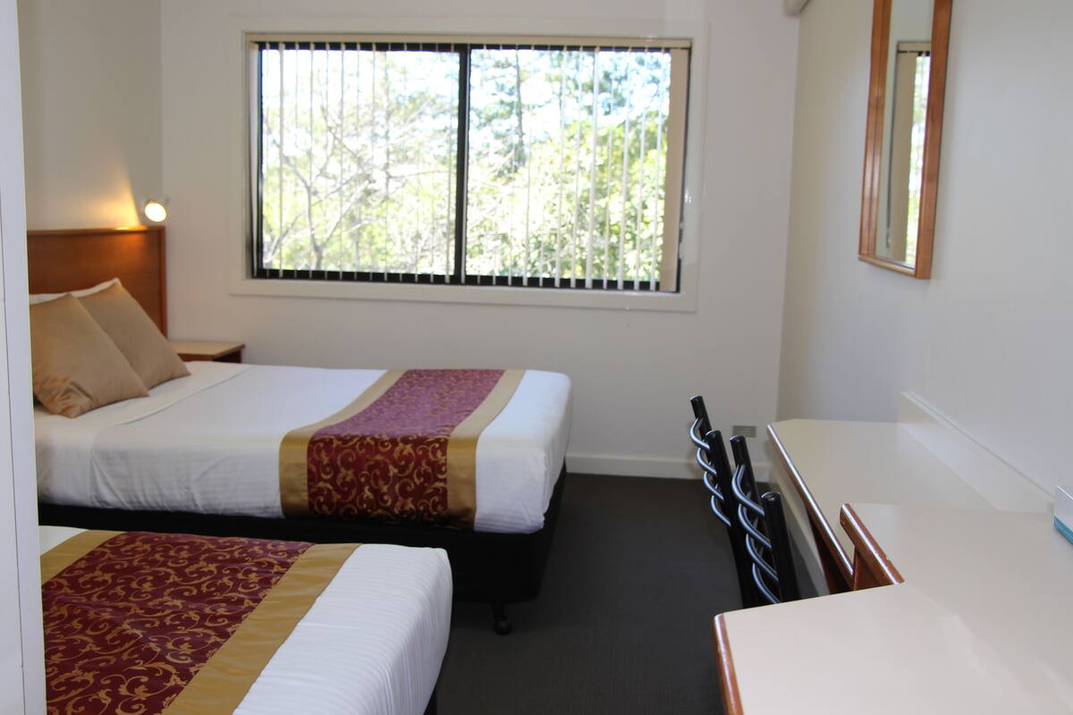A hotel room with two beds, a window with blinds, a desk, and a mirror.