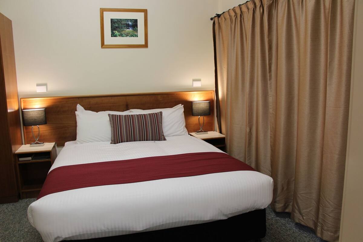 A hotel room with a large bed, two bedside tables with lamps, a framed picture on the wall, and a curtain.