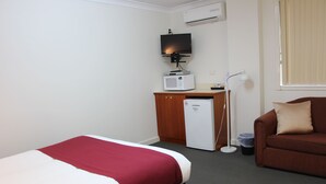 A hotel room with a bed, a desk with a microwave, a TV, a lamp, and a couch. - Pioneer Way Motel (Faulconbridge)