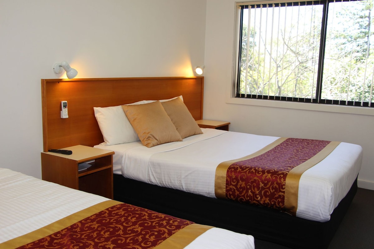 A hotel room with a bed, bedside tables, a bedside phone, and a window with blinds.