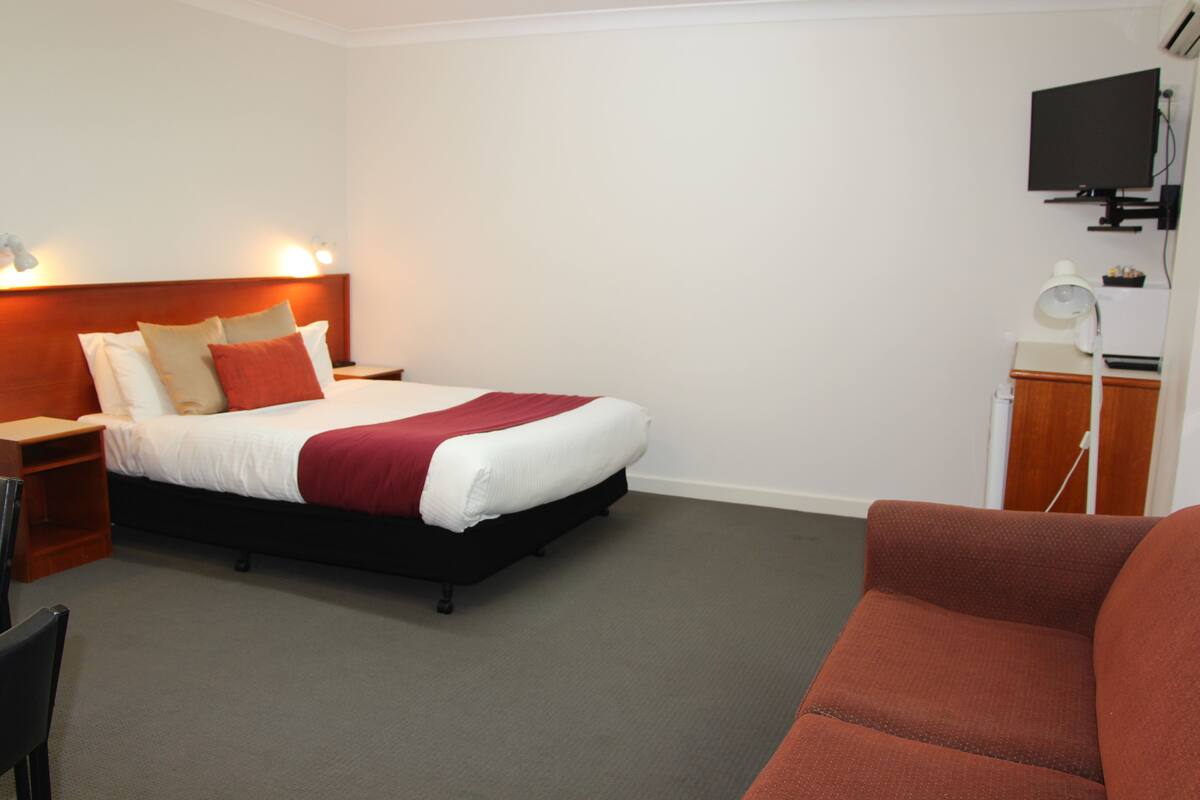 A hotel room with a bed, a desk, a chair, a TV, and a red sofa.
