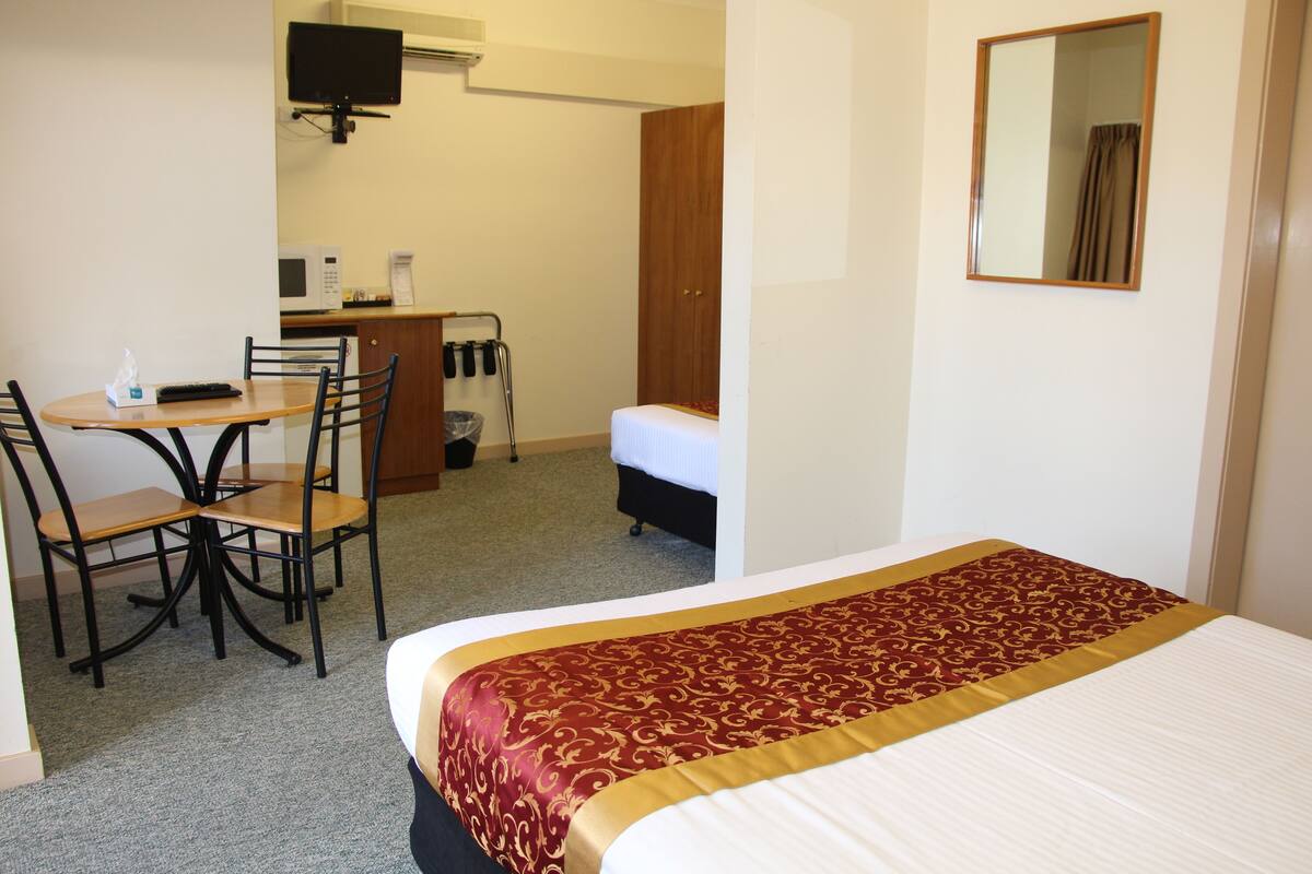 A hotel room with a bed, a desk with a chair, a television, and a wardrobe.