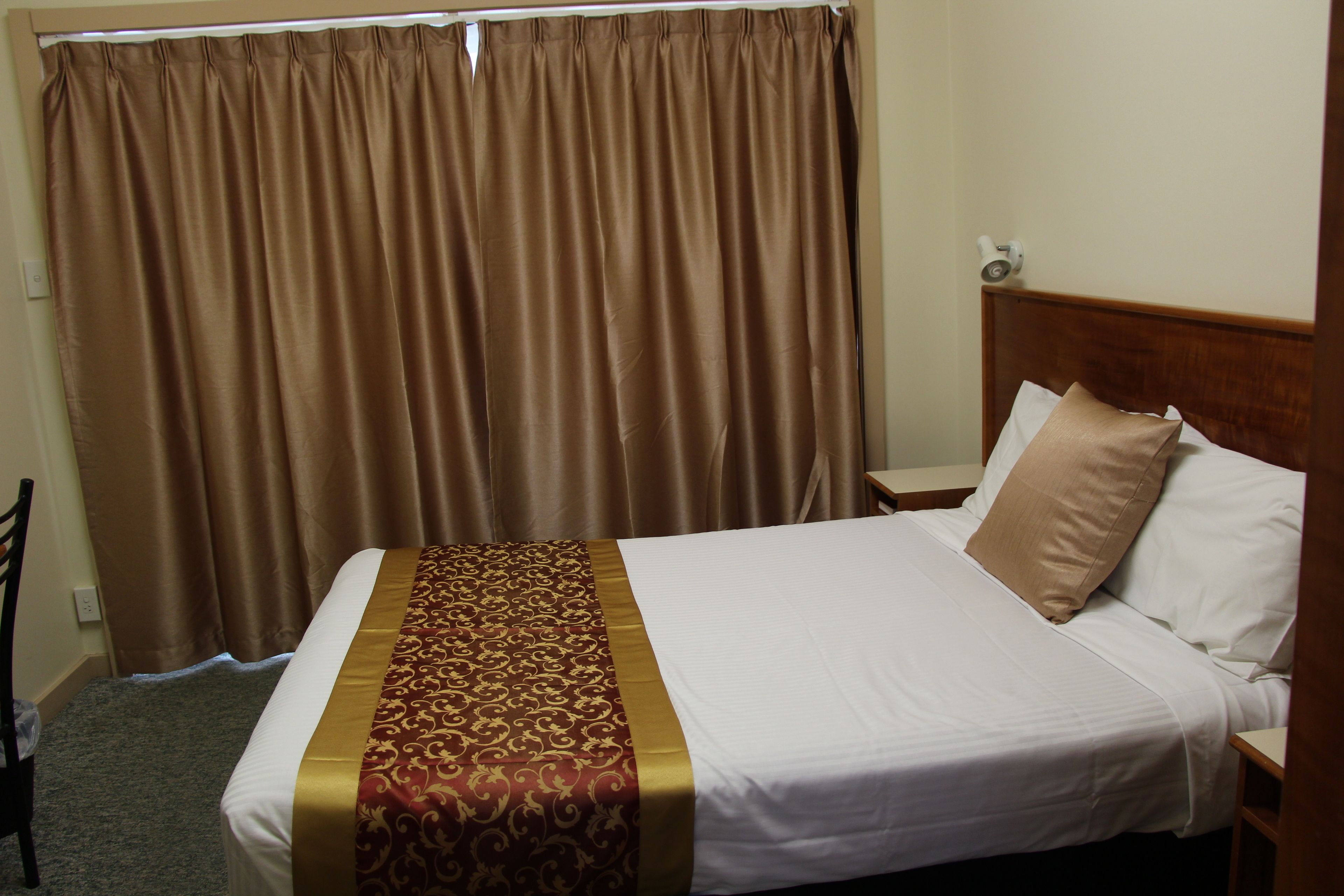 Una habitación de hotel con una cama grande, cabecero, mesita de noche y cortina.