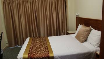 Una habitación de hotel con una cama grande, cabecero, mesita de noche y cortina.