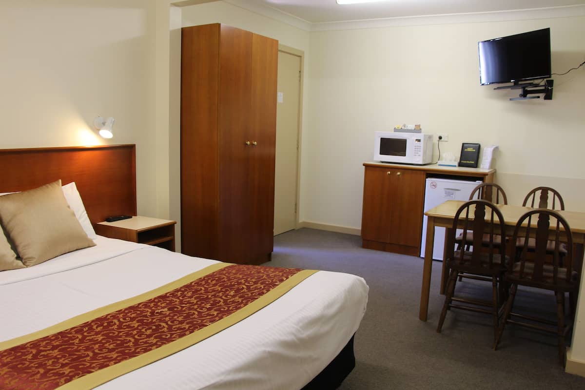 A hotel room with a bed, a desk with a microwave, a television, and a wardrobe.