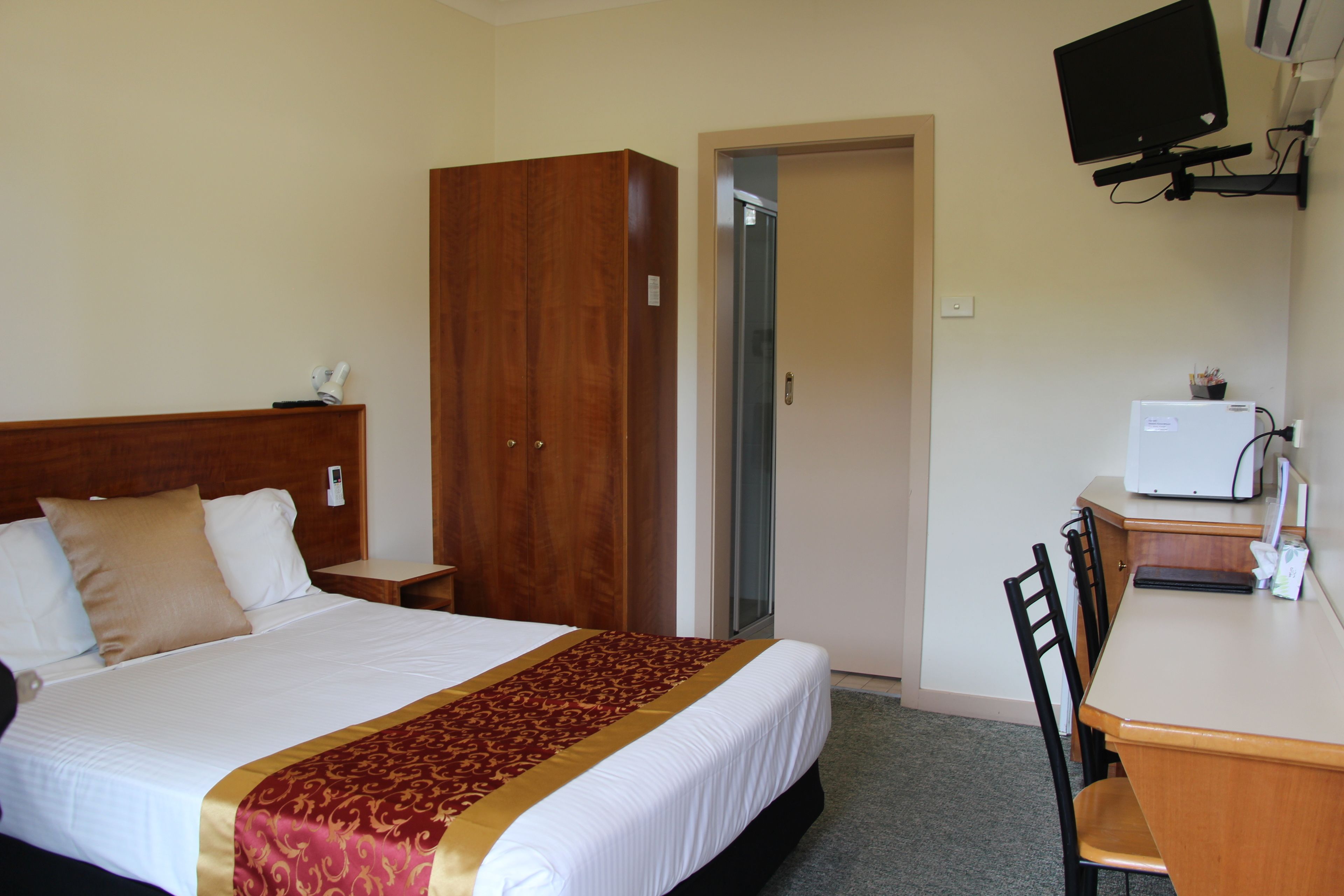 Quarto de hotel com cama, secretária, cadeira, guarda-roupa e televisão na parede.