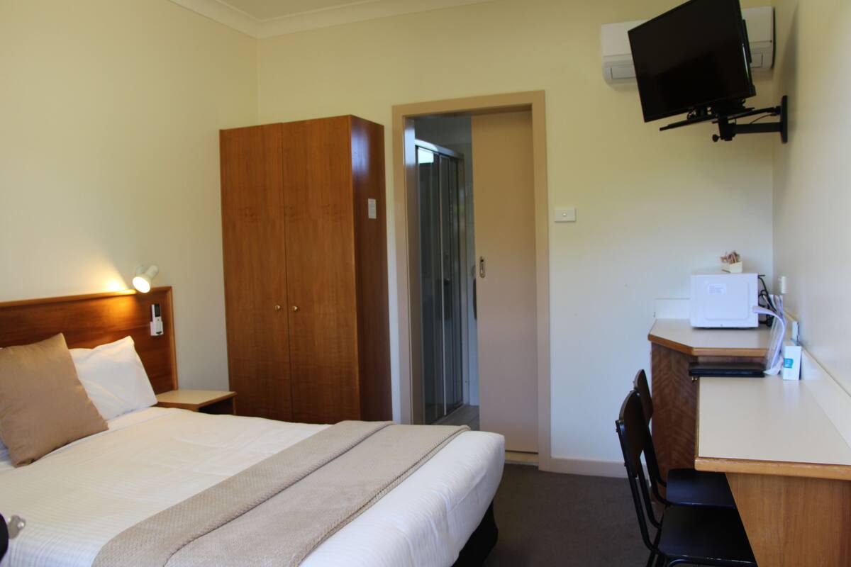 A hotel room with a bed, a desk, a chair, a wardrobe, and a television mounted on the wall.