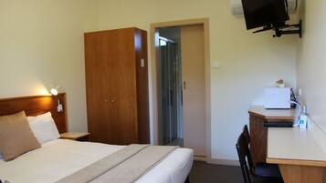 A hotel room with a bed, a desk, a chair, a wardrobe, and a television mounted on the wall.